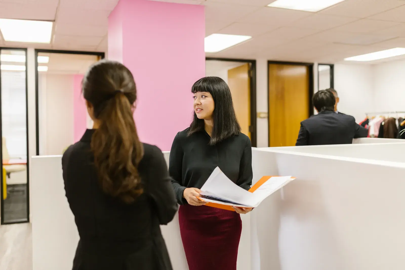 Two colleagues in business attire discuss documents in a bright office space.