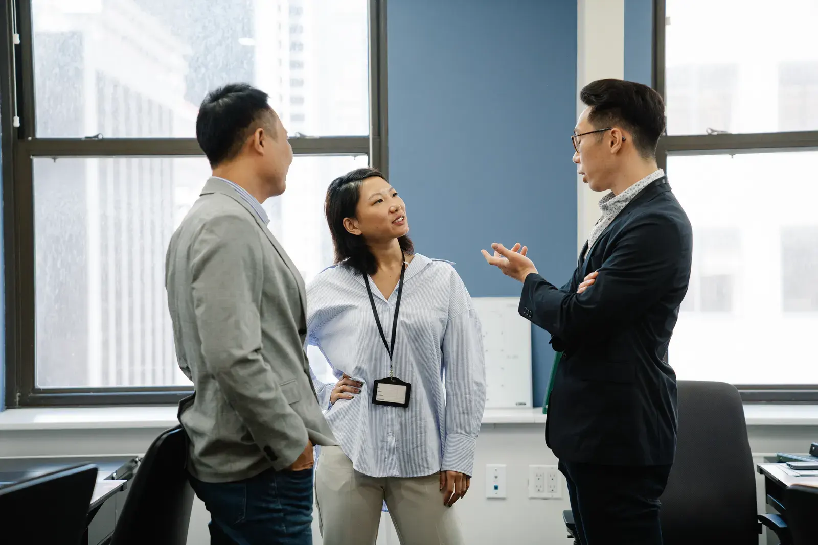 Three professional adults engaged in a lively discussion in a contemporary office environment.