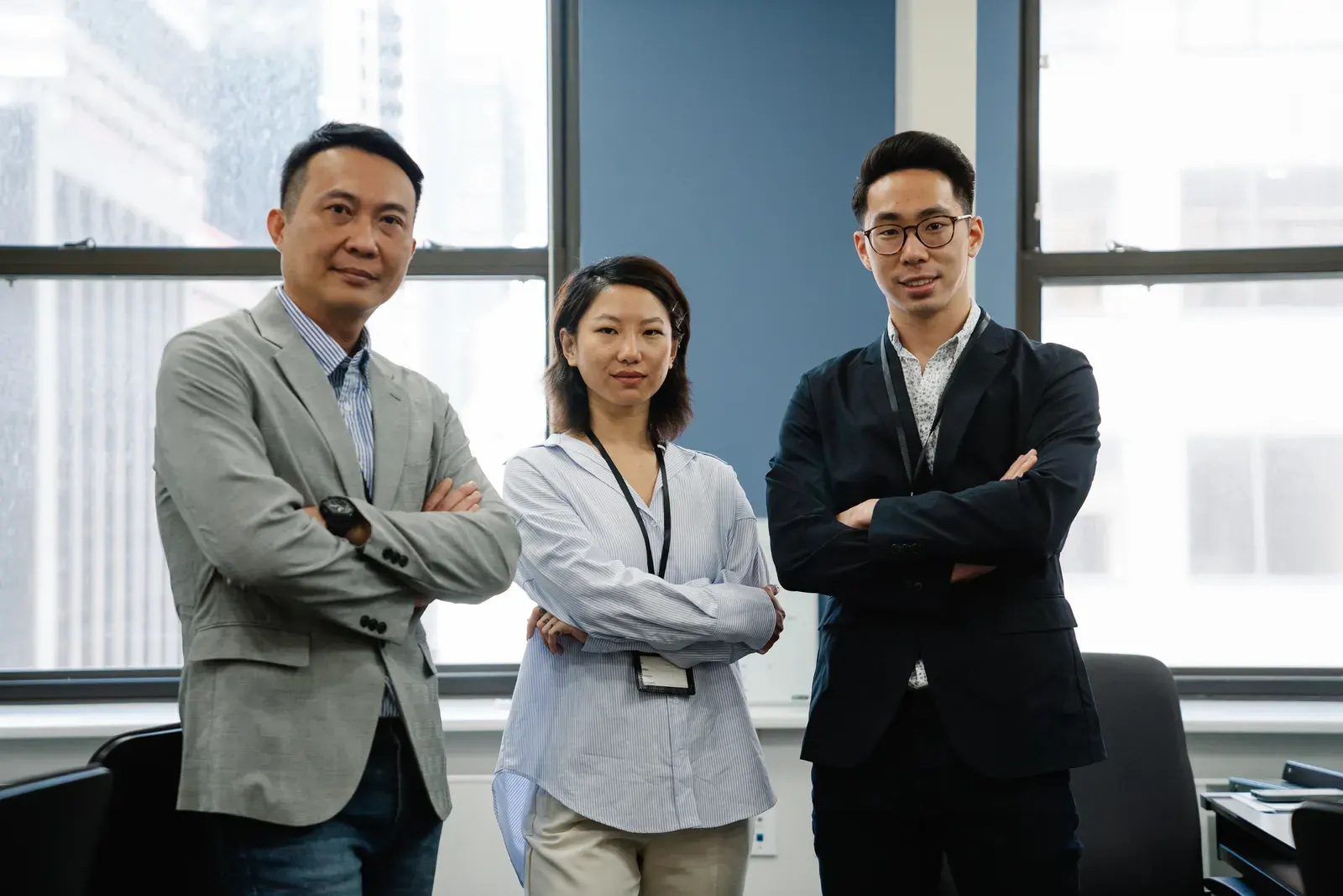 Three business professionals standing confidently with arms crossed in an urban office setting.