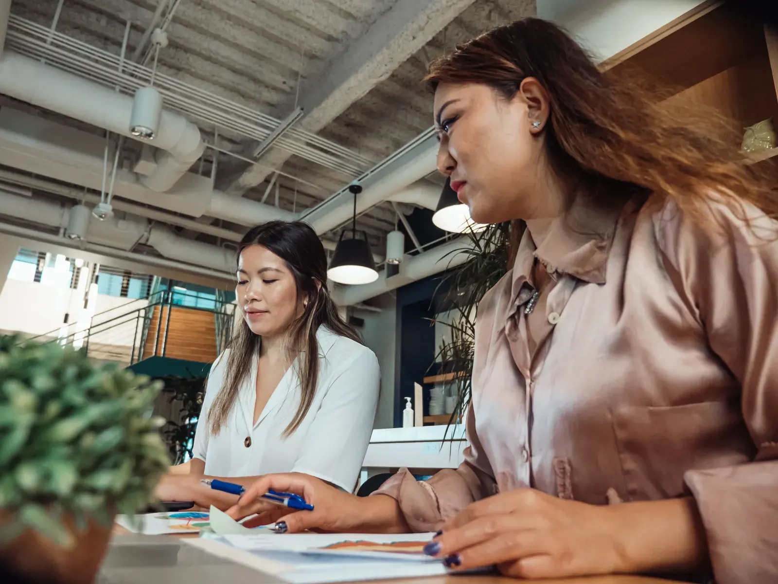 Two women collaborating at a desk in a modern office space, focusing on work tasks.