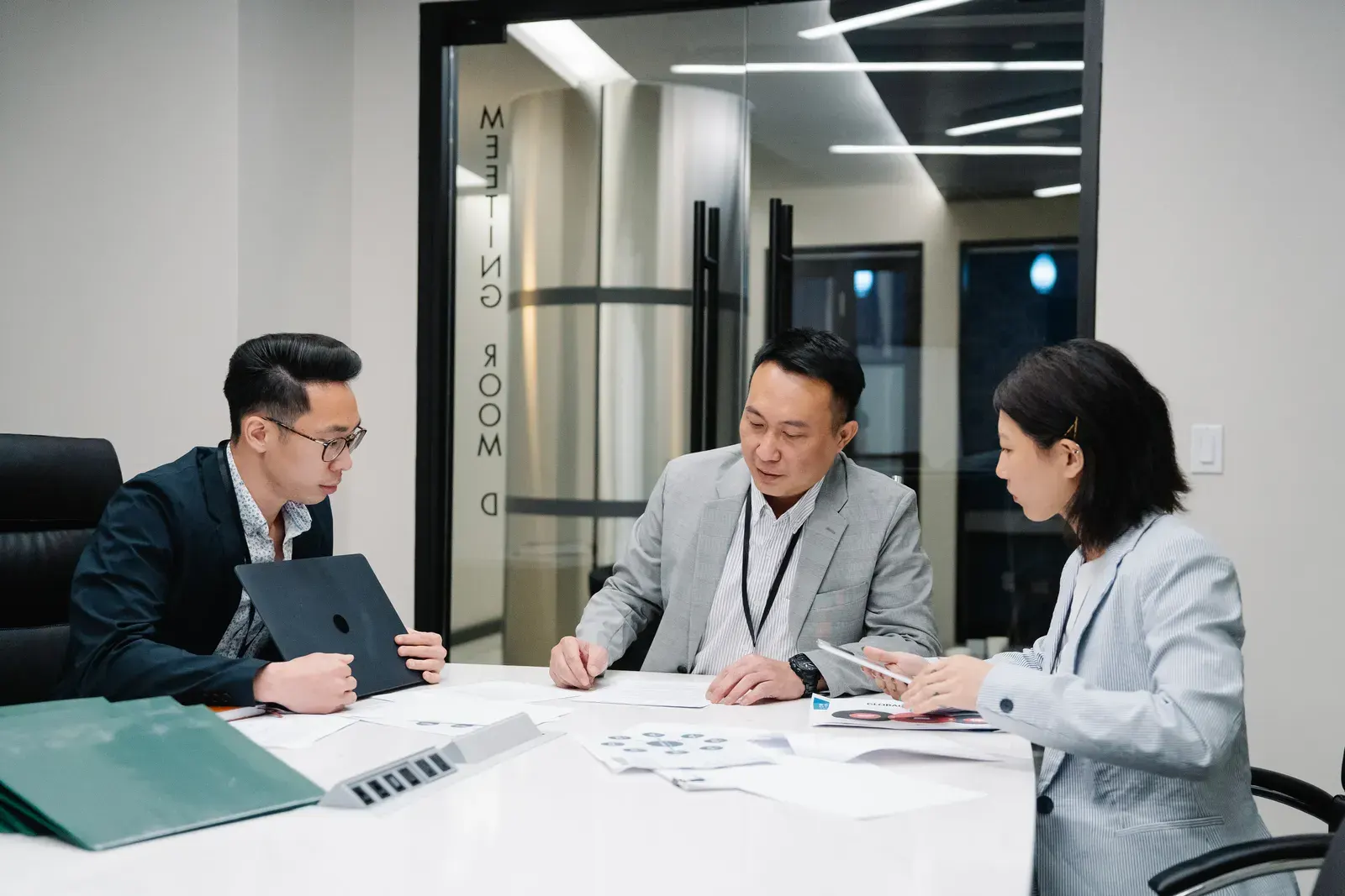 Business meeting with three professionals collaborating in a modern conference room setting.