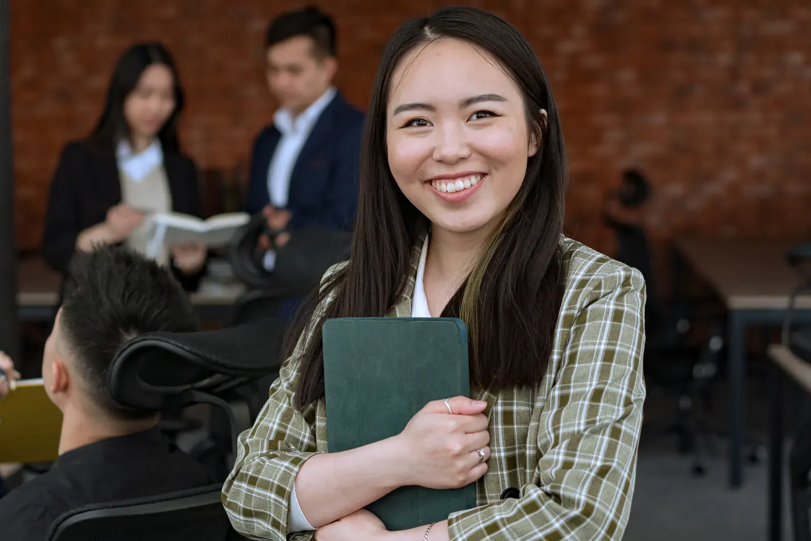 Smiling woman in a professional office environment holding a tablet, conveying confidence and professionalism.