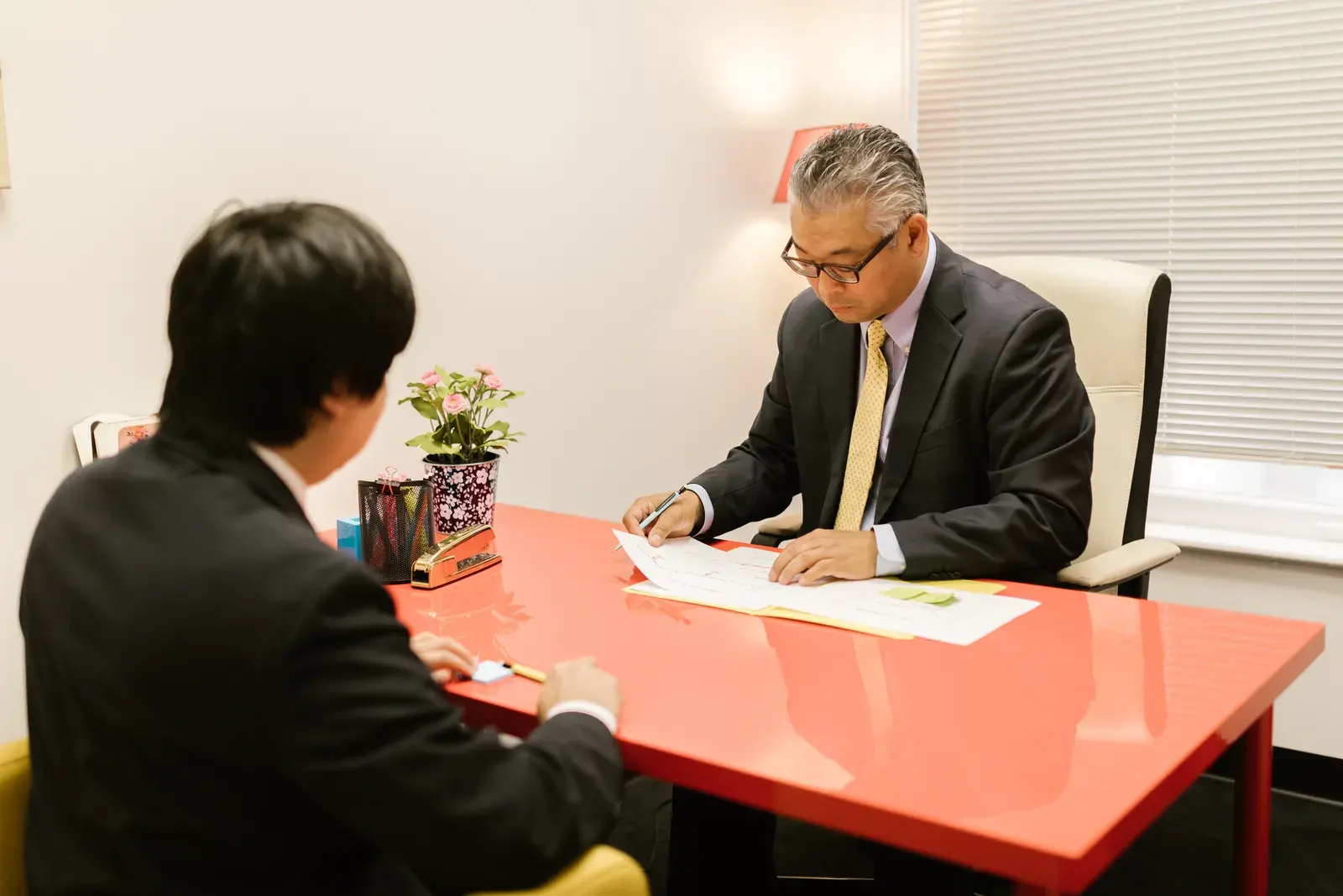 Two professionals discussing documents in a modern office with a red desk.