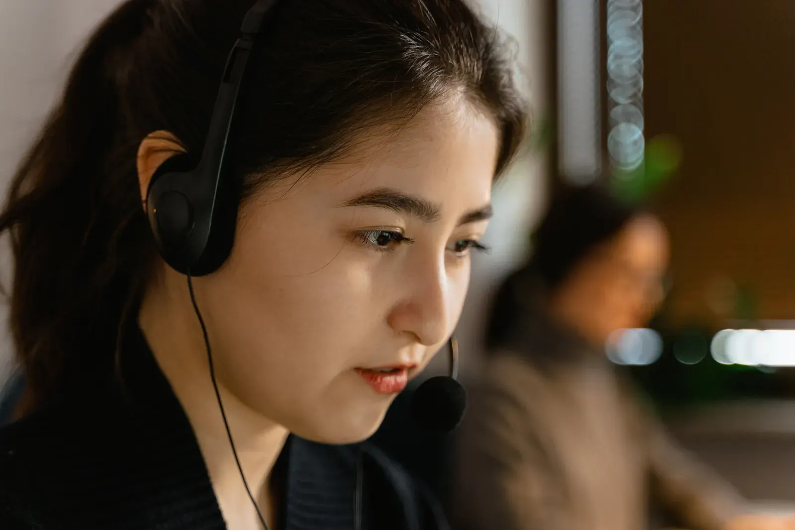 Focused Asian woman in headset providing customer support in office setting.