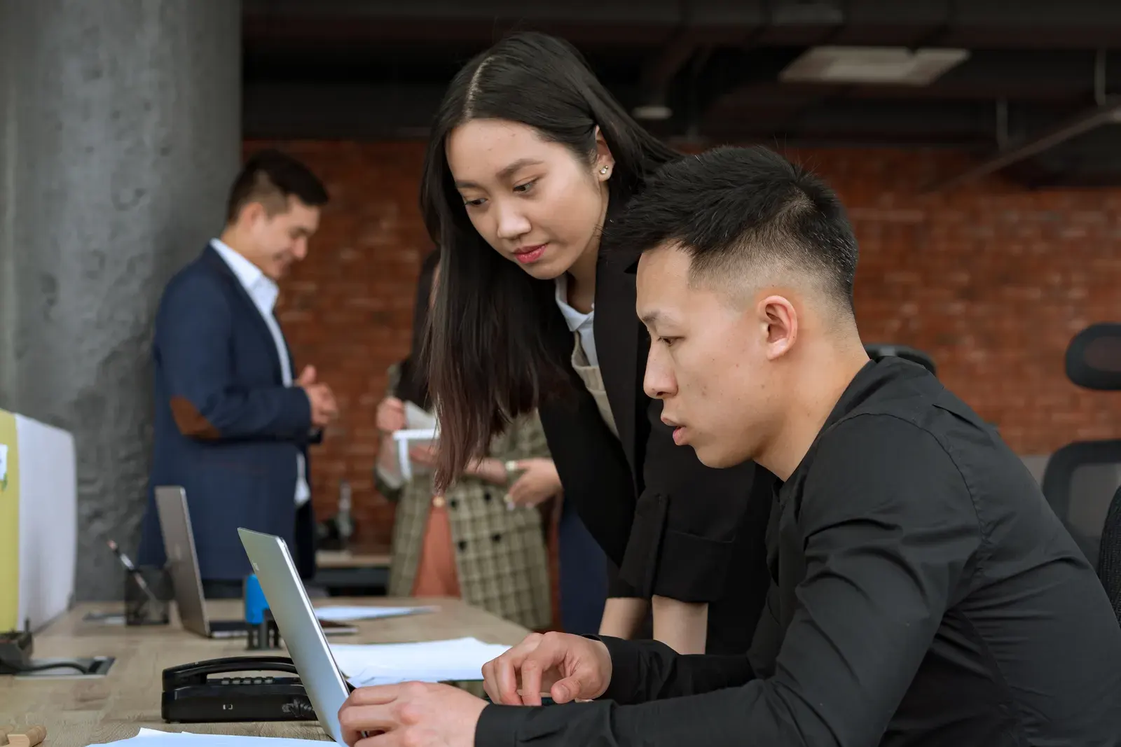 Professionals working together in a modern office setting around a laptop.