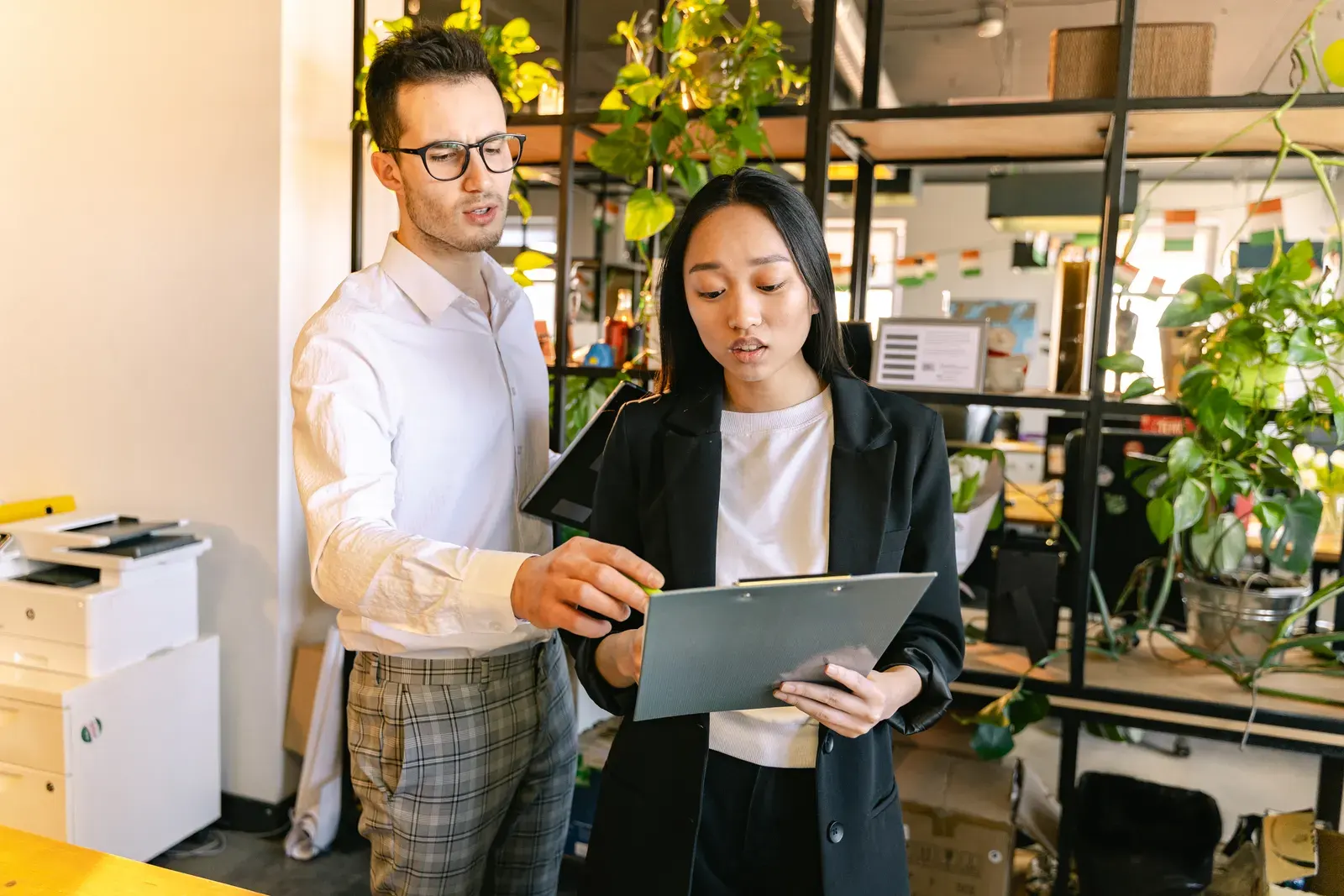 A man and woman collaborating on a project in a modern office setting with plants.