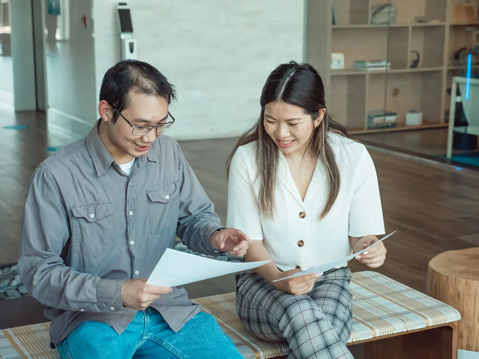 Two colleagues having a discussion while reviewing documents in a modern office setting.