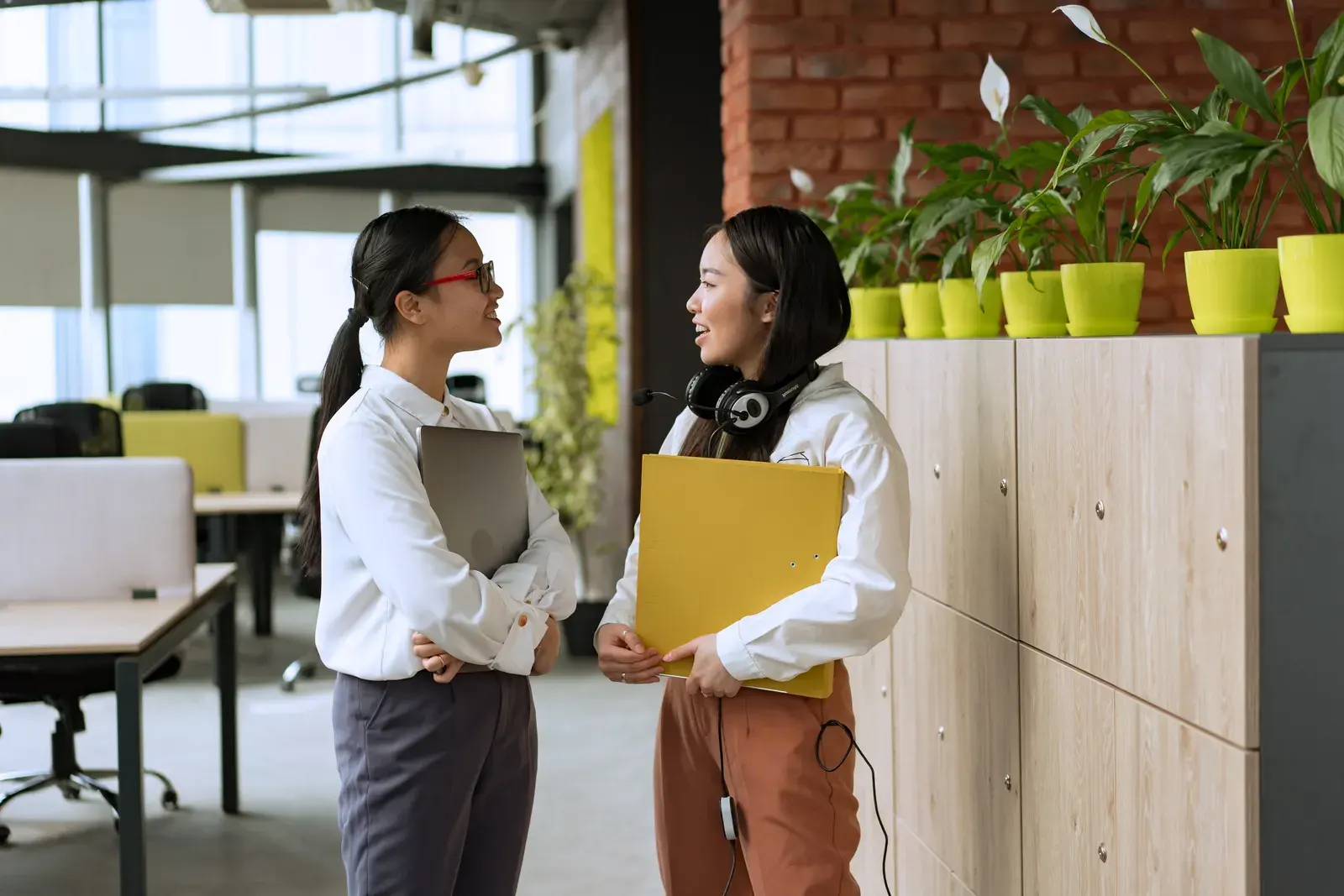 Two young professional women engaging in a conversation in a modern office setting.