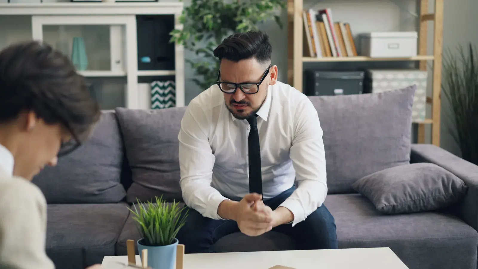 A stressed businessman in therapy session, showing visible emotions on a sofa.