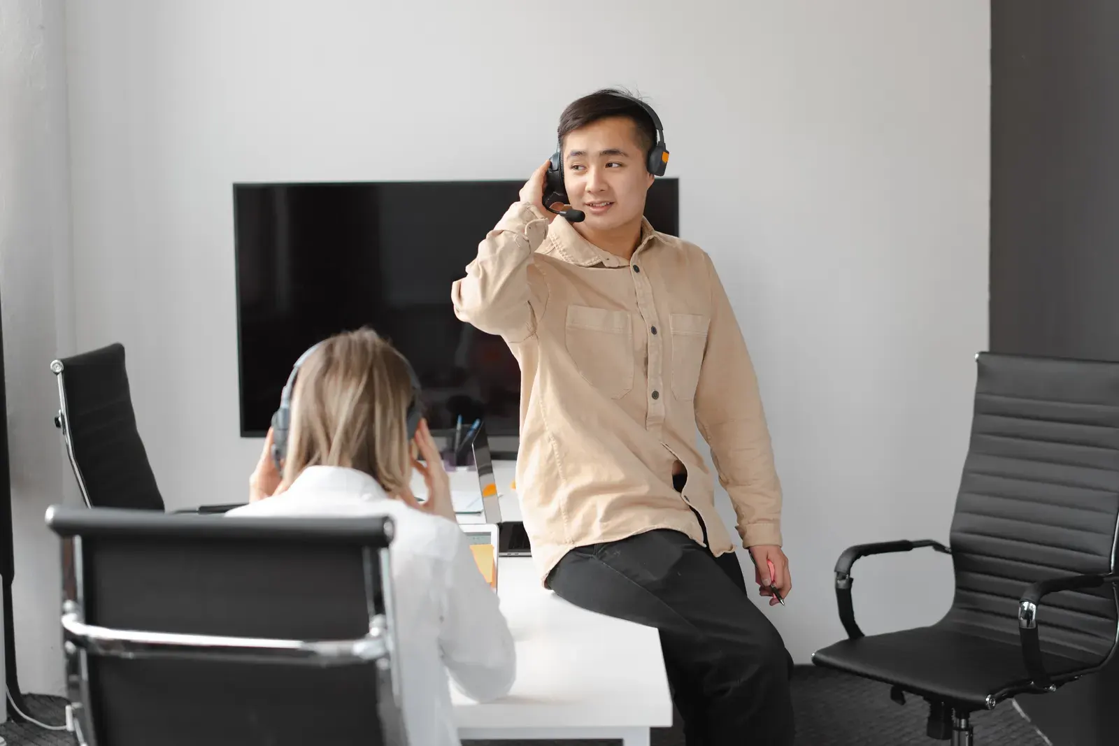 Two colleagues in an office setting using headsets for communication, suggesting teamwork.