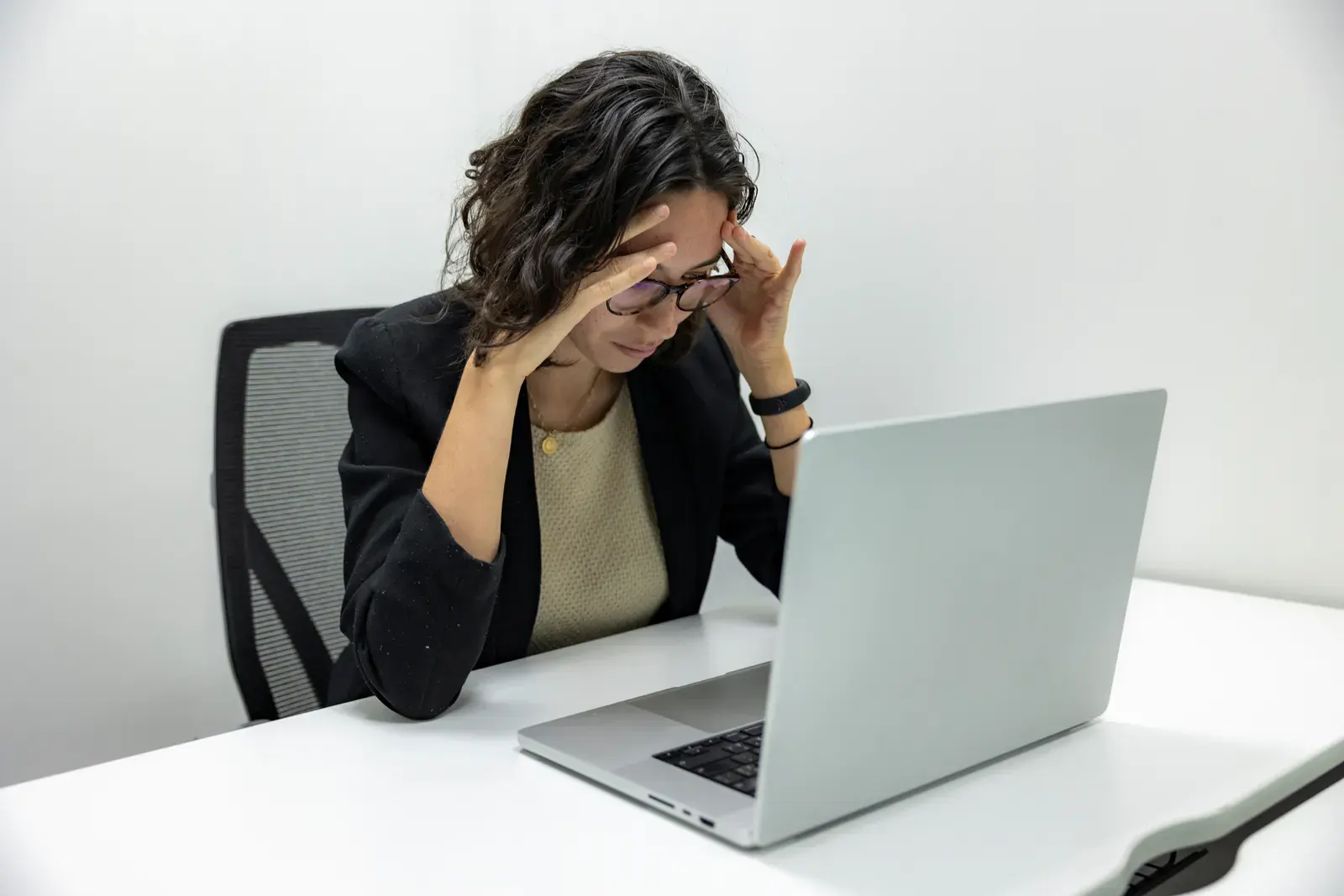 A young woman experiencing stress and fatigue while working on her laptop in an office setting.
