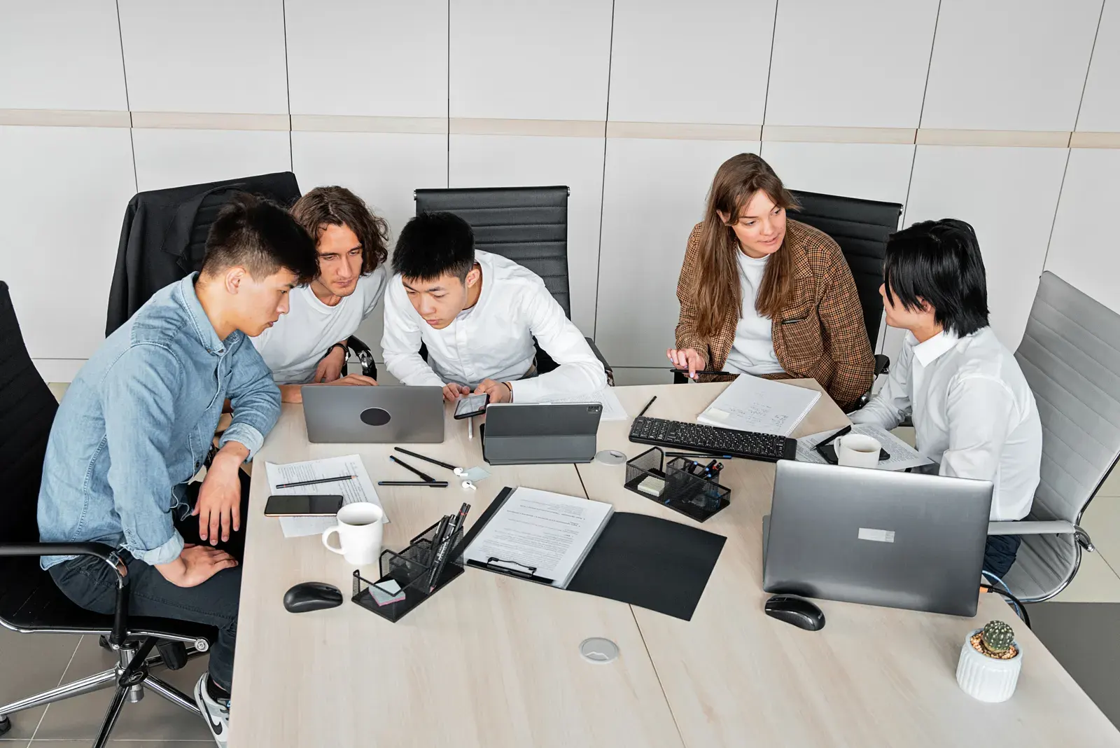 A diverse group of colleagues working together in an office setting with laptops and documents.