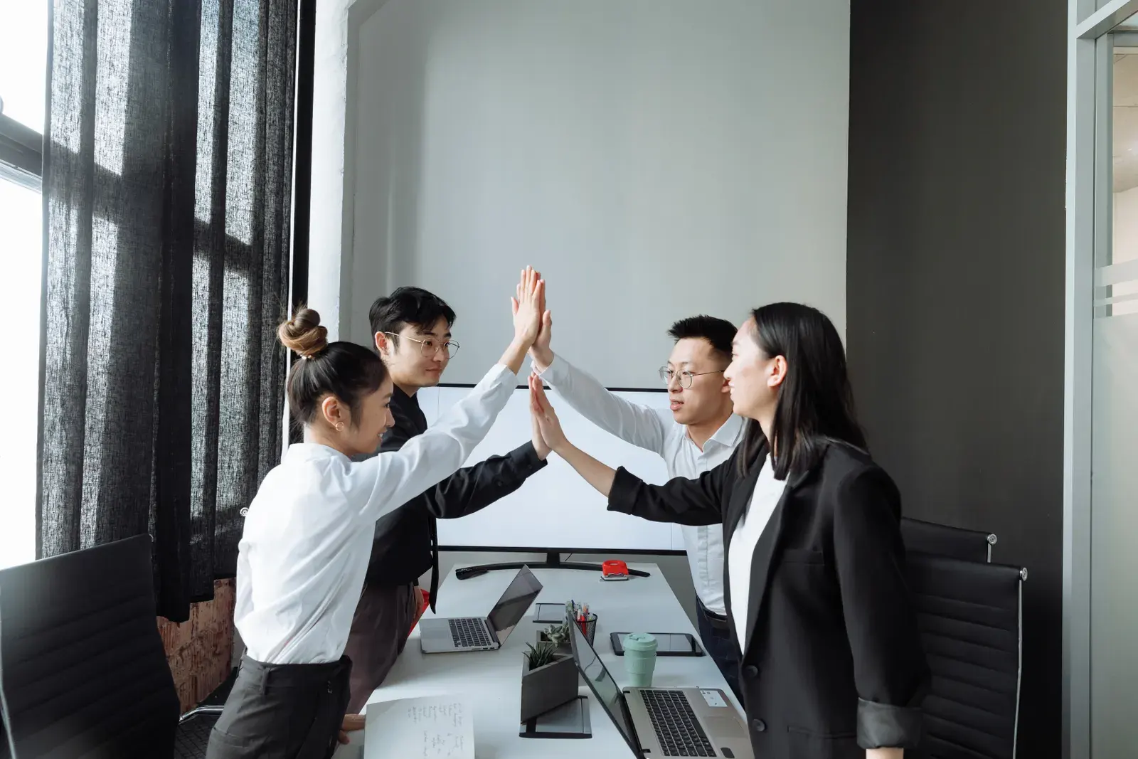 Four colleagues in a modern office high-fiving, celebrating teamwork and success.