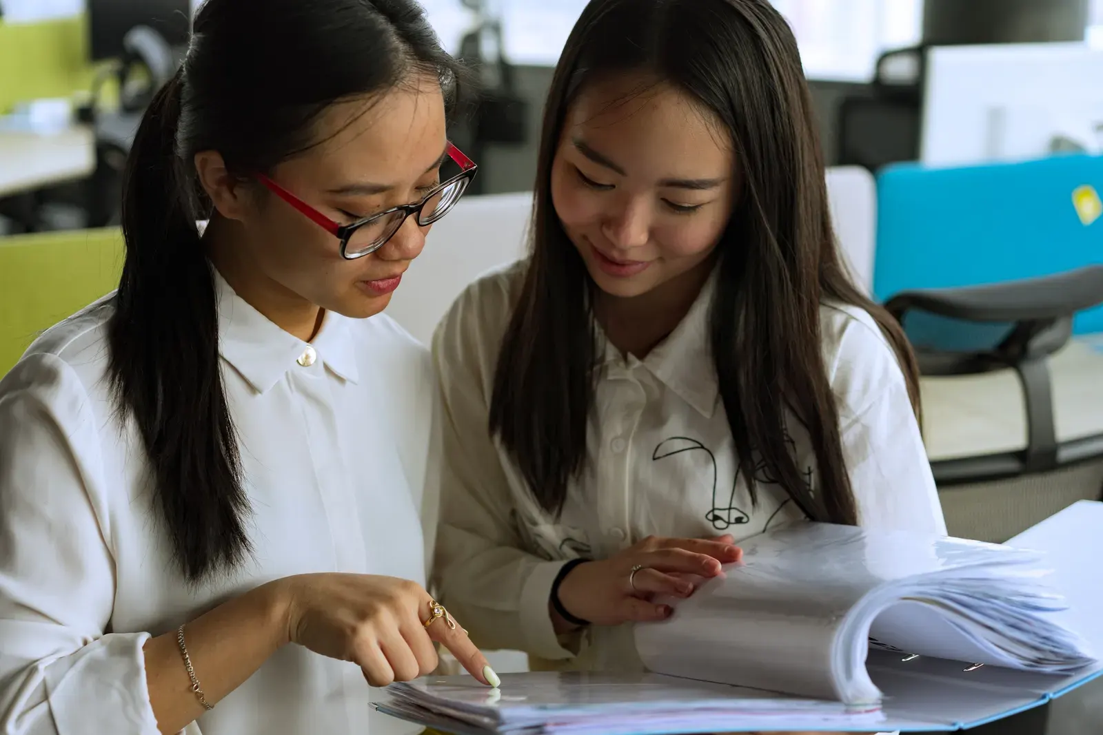 Two young women collaborating on a project in a modern office environment, emphasizing teamwork and productivity.