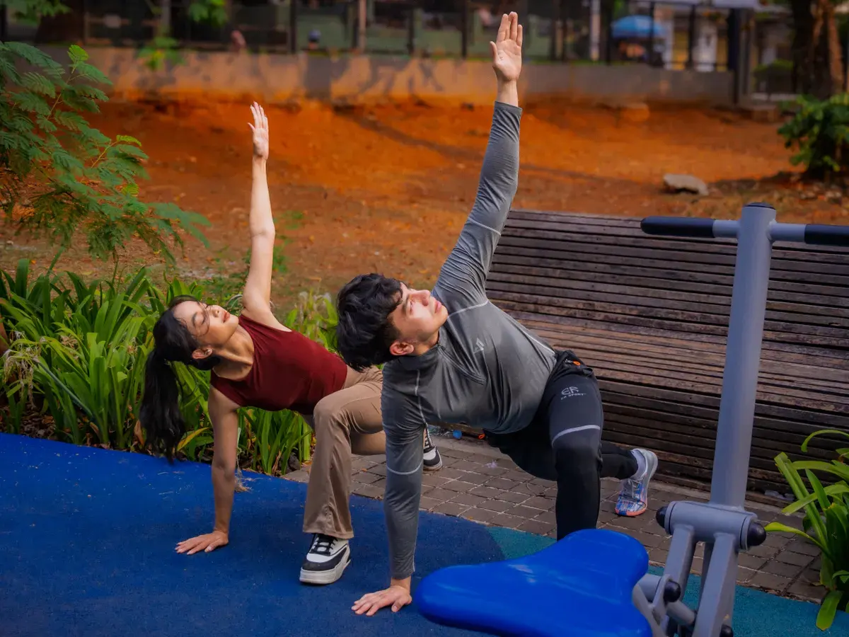 Two adults practicing yoga outdoors in Jakarta's vibrant setting, promoting health and fitness.