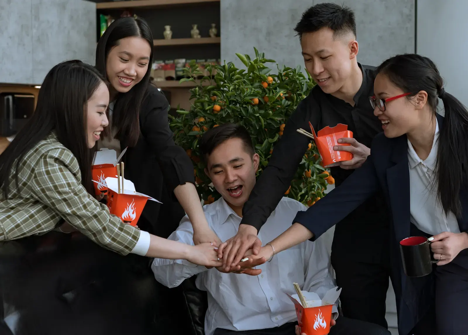 Group of coworkers enjoying a lunch break, stacking hands for teamwork in an office setting.