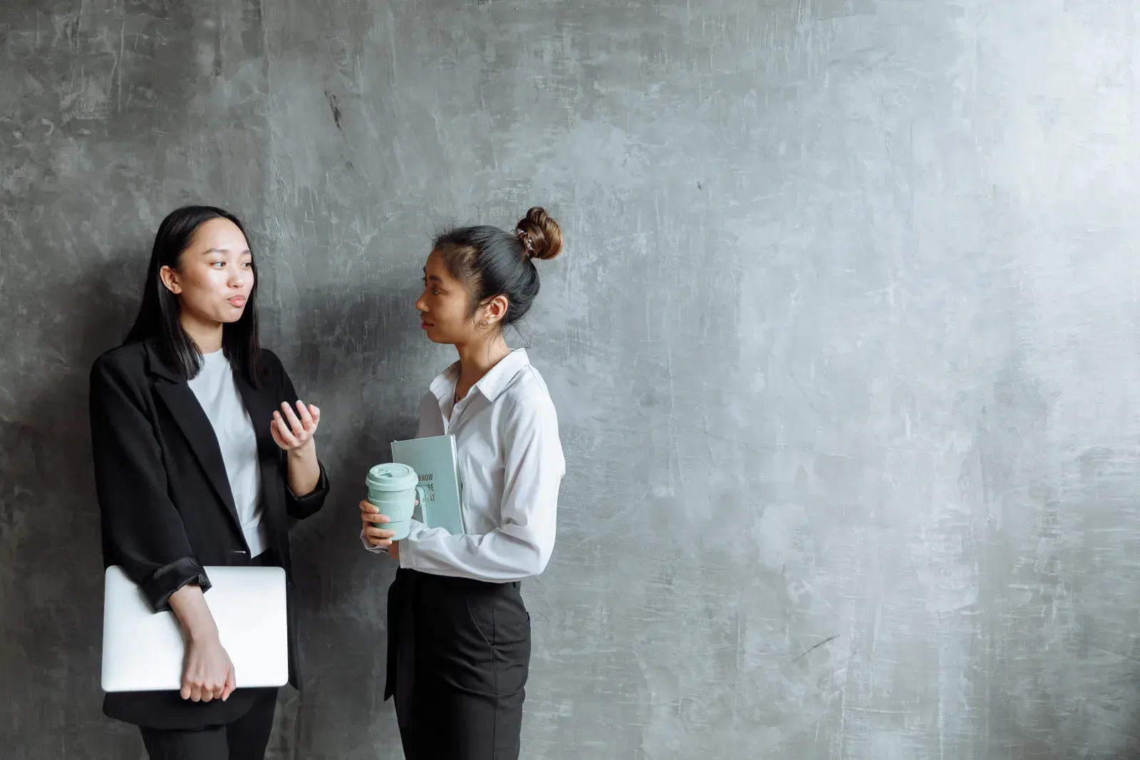 Two businesswomen discussing work in a minimalist, modern office environment.