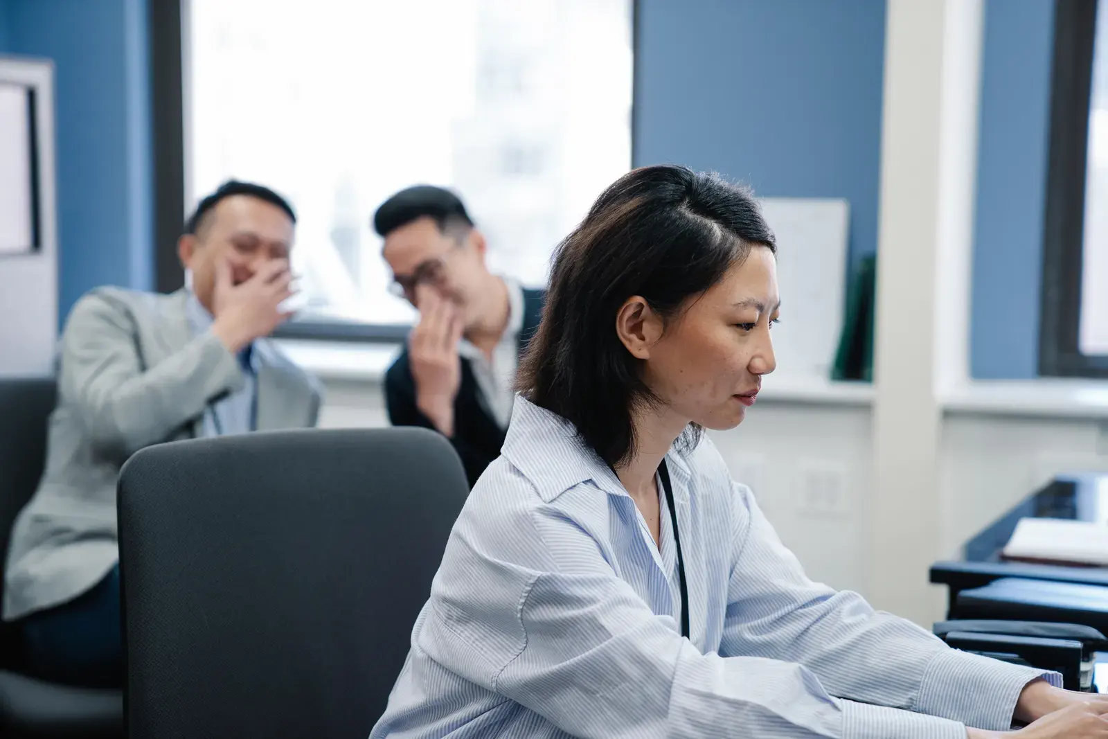 Focused office worker with colleagues gossiping in the background, showcasing workplace dynamics.